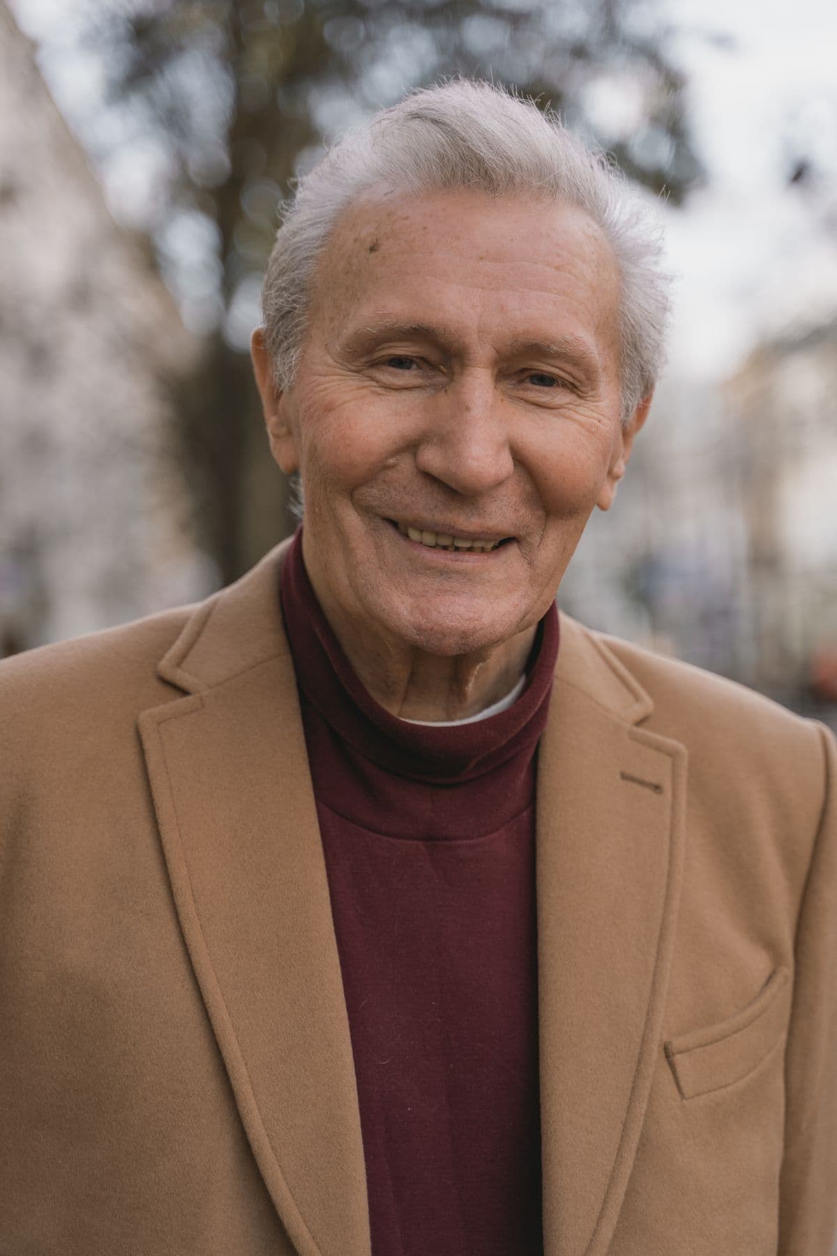 Older man in a tan coat standing outdoors